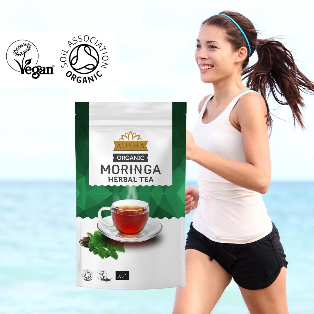 Organic Moringa Tea 100g package with vegan and organic certification, smiling woman exercising in the background.