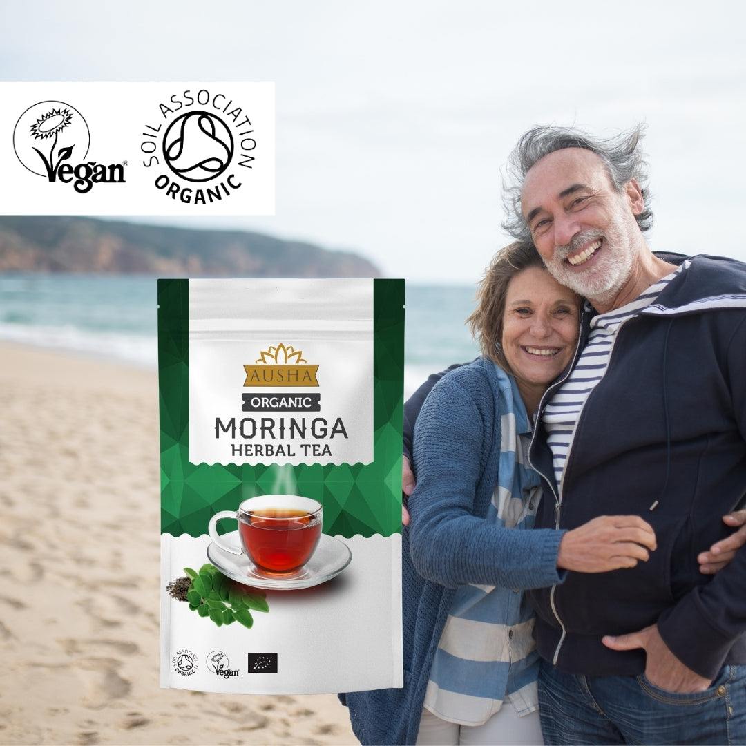 Organic Moringa Tea pack on a beach, featuring vegan and organic certification logos.