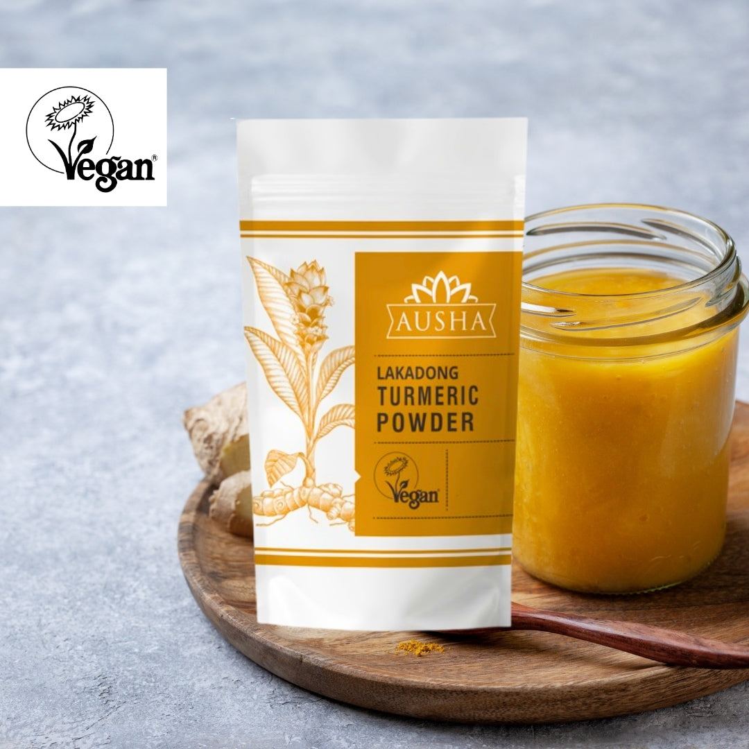Lakadong Turmeric Powder in a vegan-branded pouch with a jar of turmeric paste on a wooden board.