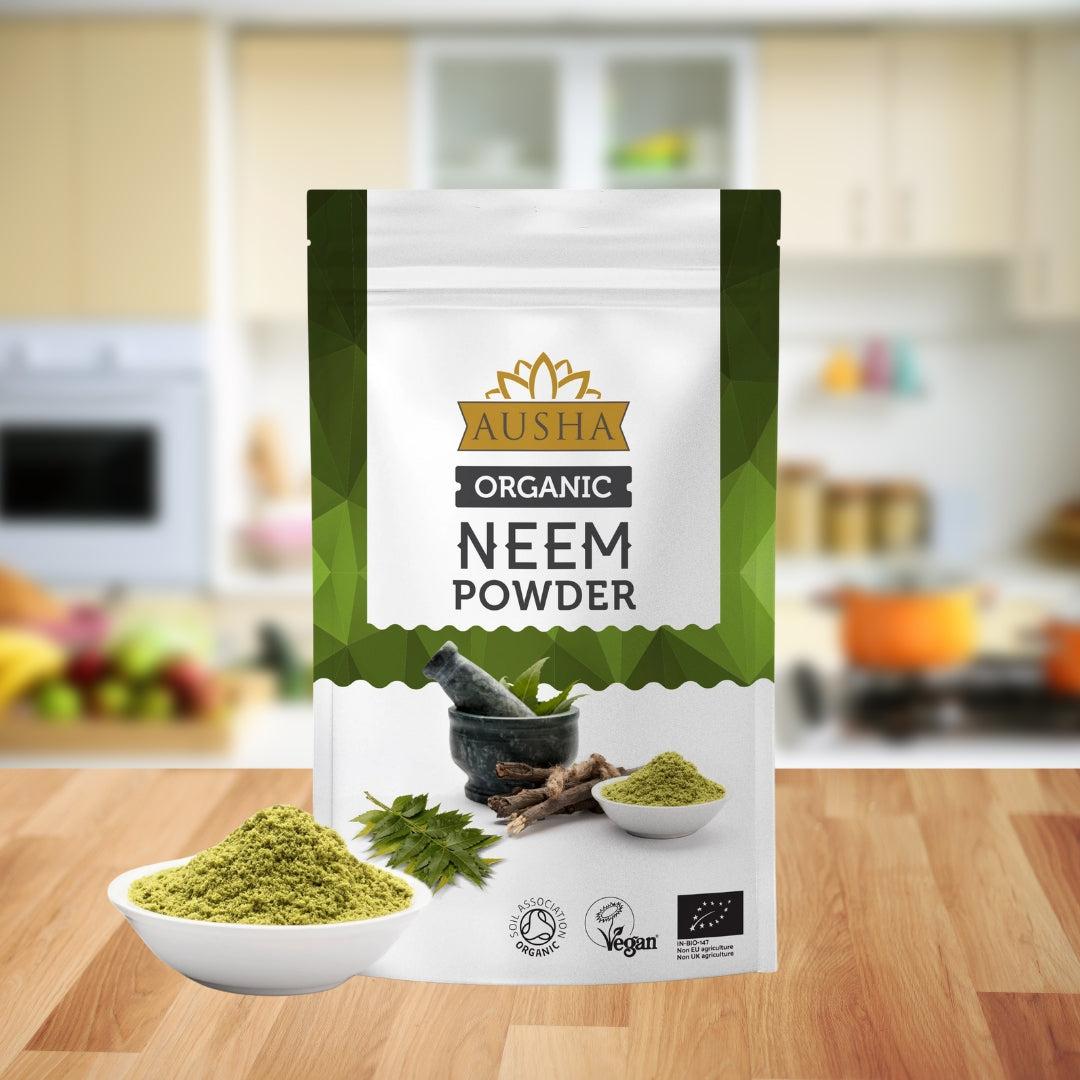 Organic Neem Powder in a sealed package with bowls of green powder and neem leaves displayed on a kitchen counter.
