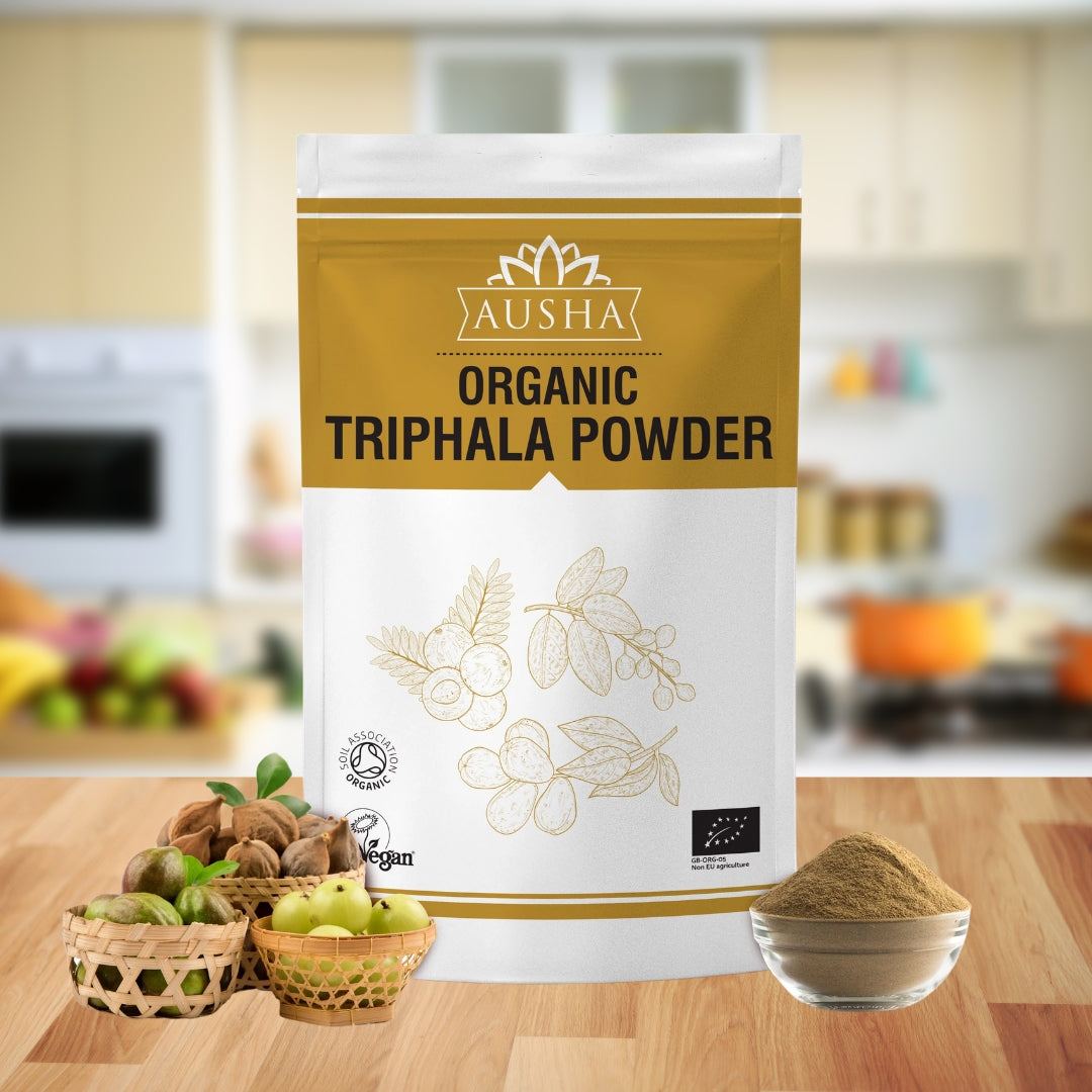 Organic Triphala Powder packaging on kitchen counter with bowls of fruits and powder.