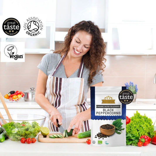 Organic Salted Telicherry Black Peppercorns 100g package in kitchen setting with certification logos.
