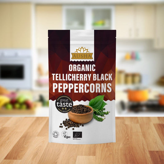 Organic Tellicherry Black Peppercorns in a kitchen setting, featuring a branded package and fresh peppercorns in a wooden bowl.