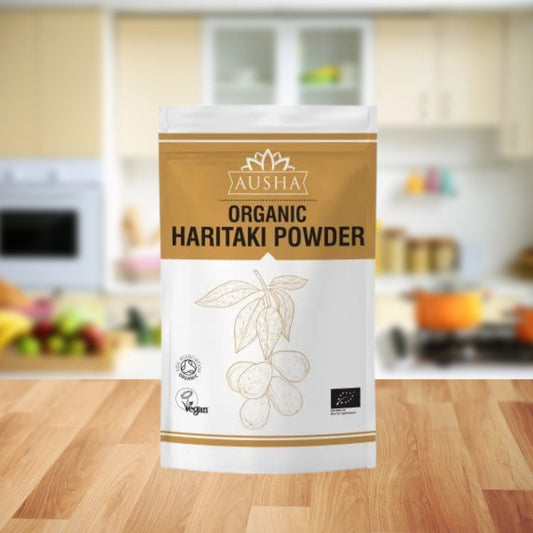 Organic Haritaki Powder 100g package on a kitchen counter, featuring eco-friendly and vegan certifications.