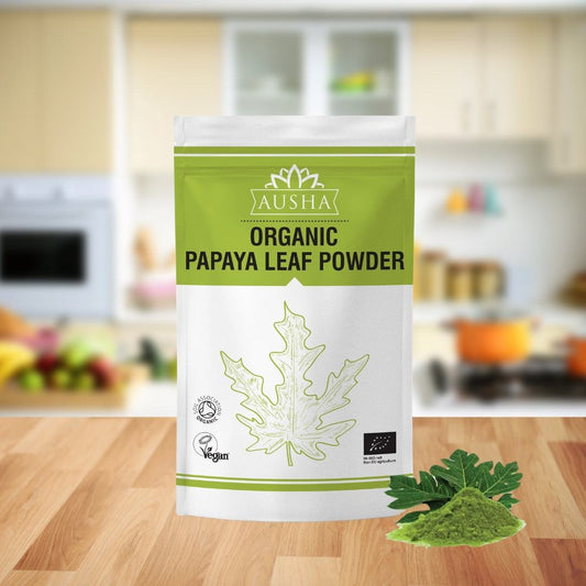 Organic Papaya Leaf Powder 100g pack on kitchen counter with dried green powder nearby.