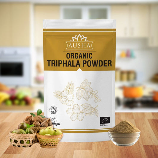 Organic Triphala Powder packaging on kitchen counter with bowls of fruits and powder.